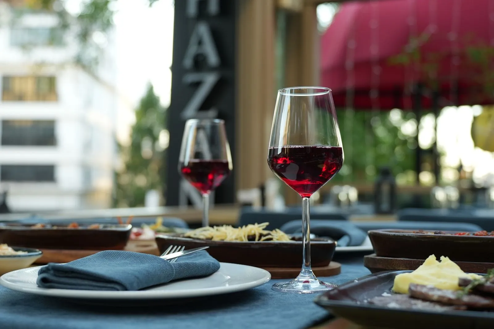 A sophisticated dining setup featuring red wine, gourmet dishes, and a casual outdoor atmosphere.
